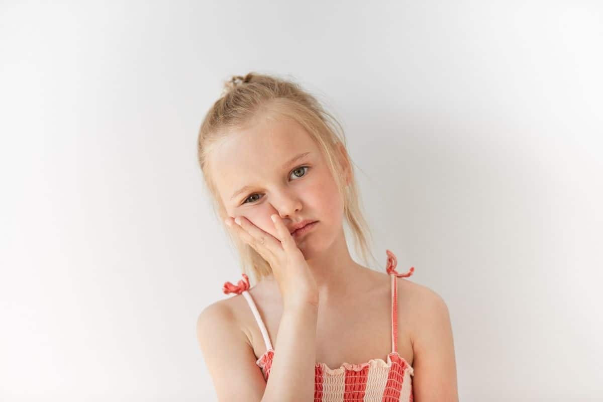 Young girl with hand to cheek showing signs of jaw discomfort or TMJ pain.