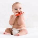 Happy baby chewing on red teething toy, illustrating common infant teeth grinding behavior.