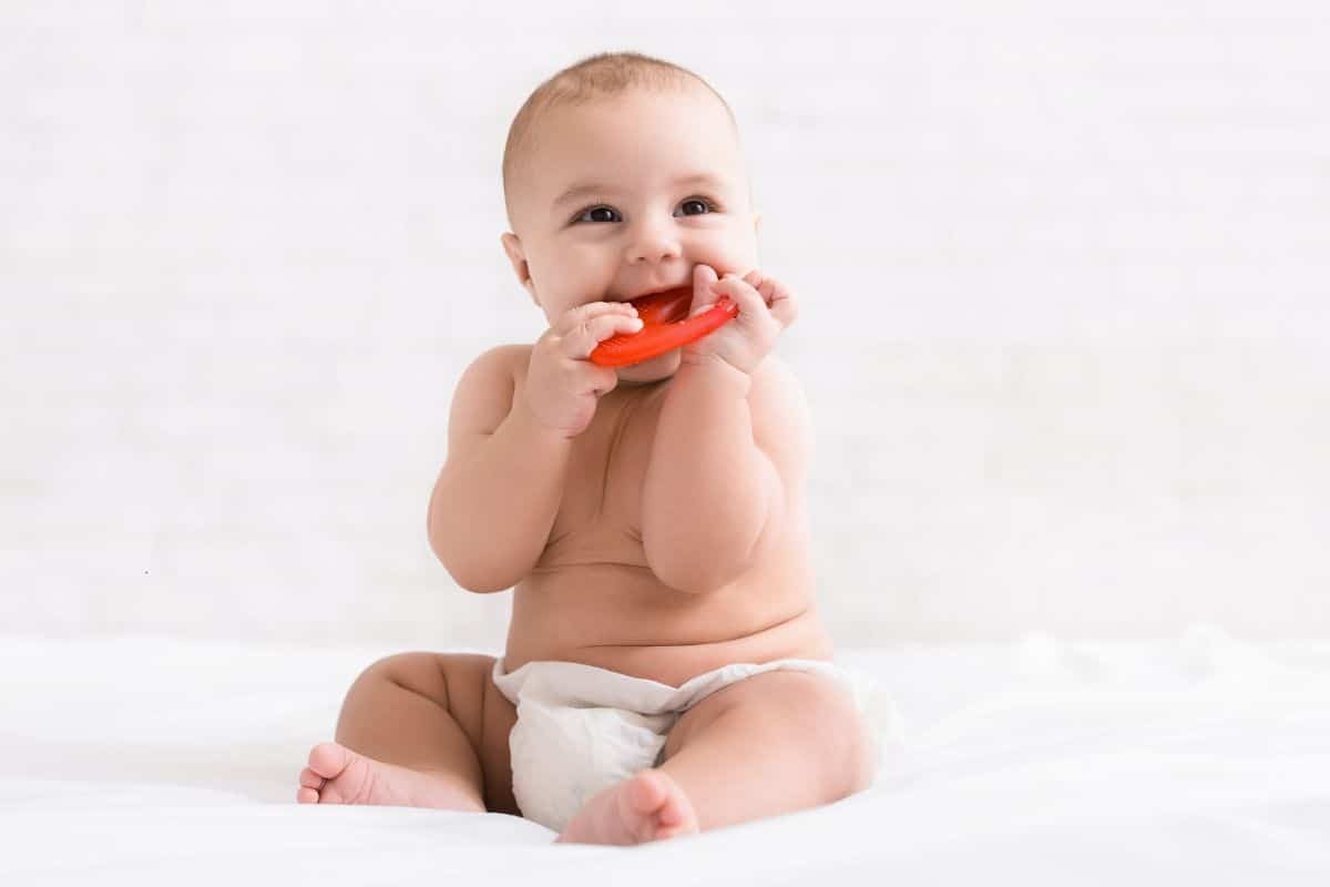 Happy baby chewing on red teething toy, illustrating common infant teeth grinding behavior.