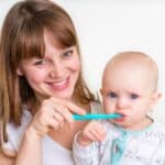 Older sister helping young toddler brush teeth with blue toothbrush.