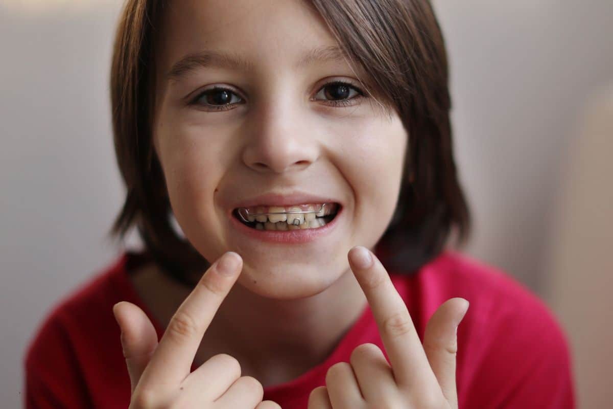 Child with metal braces smiling and pointing to teeth in Spring, TX dental practice.