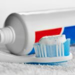 Toothbrush with white and blue bristles topped with fluoride toothpaste next to a tube.