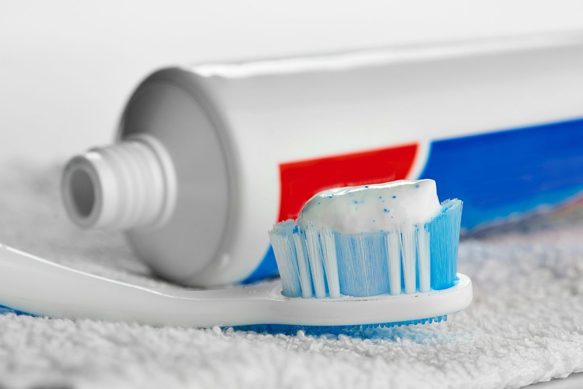 Toothbrush with white and blue bristles topped with fluoride toothpaste next to a tube.