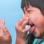 Child covering mouth with hand while showing signs of bad breath concern.