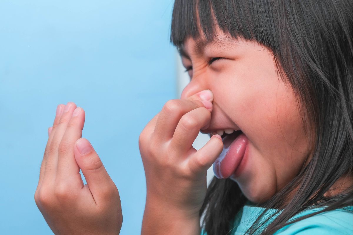 Child covering mouth with hand while showing signs of bad breath concern.