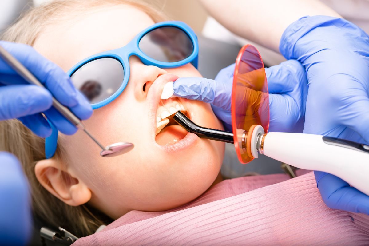 Young patient wearing blue protective glasses during dental filling procedure with dentist.