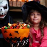 Kids in Halloween costumes with a jack-o-lantern candy bowl containing cavity-friendly treats.