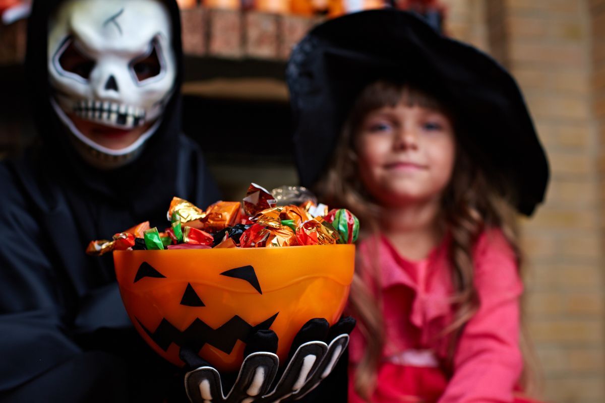 Kids in Halloween costumes with a jack-o-lantern candy bowl containing cavity-friendly treats.