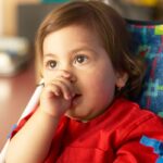 Young child in red shirt sitting in dental chair with colorful patterned headrest during pediatric dental visit.