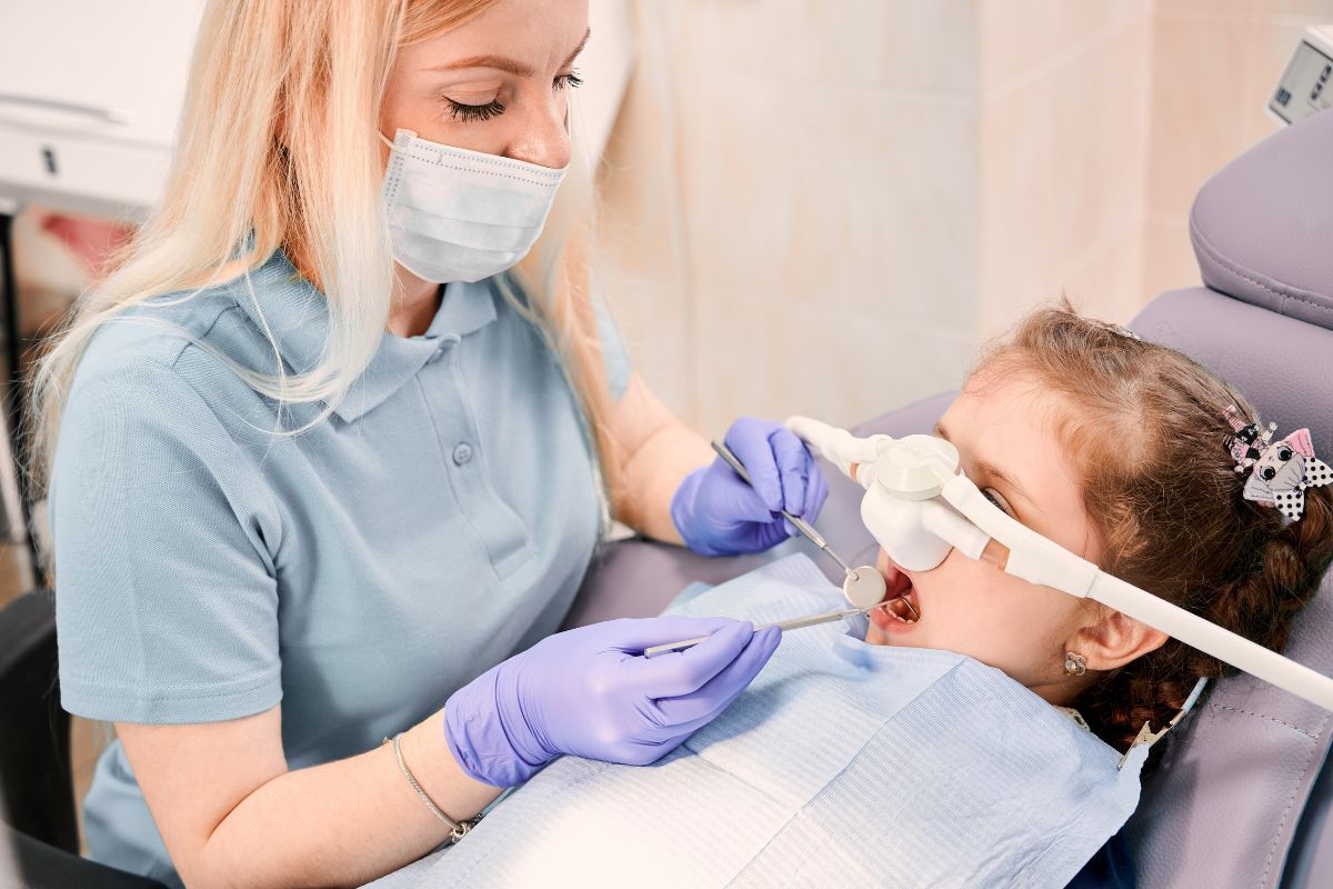 Pediatric dentist examining young patient's teeth during dental procedure with protective eyewear.