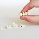 Hand holding dental crown next to scattered crowns on white surface.