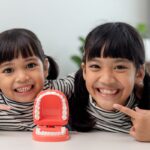 Two smiling children with a dental model showing teeth, demonstrating pediatric dental health education.