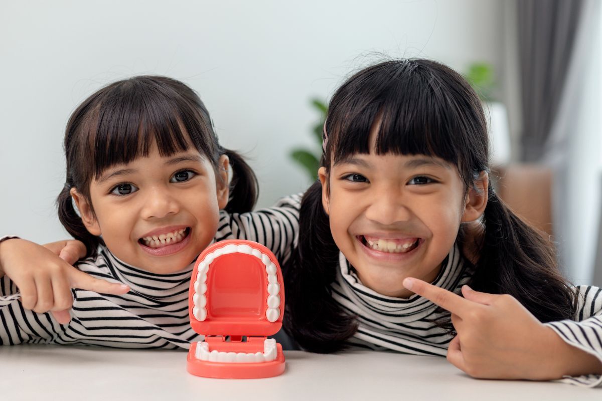 Two smiling children with a dental model showing teeth, demonstrating pediatric dental health education.