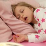 Young child sleeping peacefully in pink bedding, wearing star-patterned pajamas, depicting restful sleep.