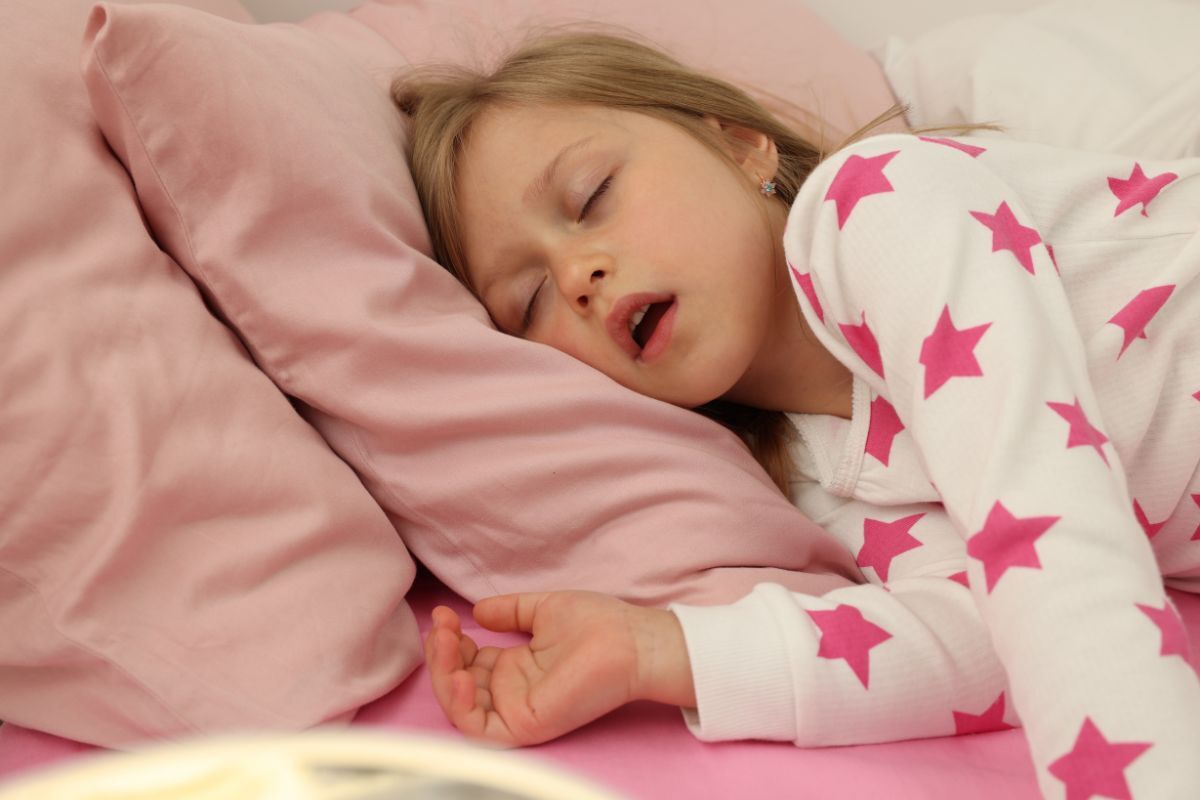 Young child sleeping peacefully in pink bedding, wearing star-patterned pajamas, depicting restful sleep.