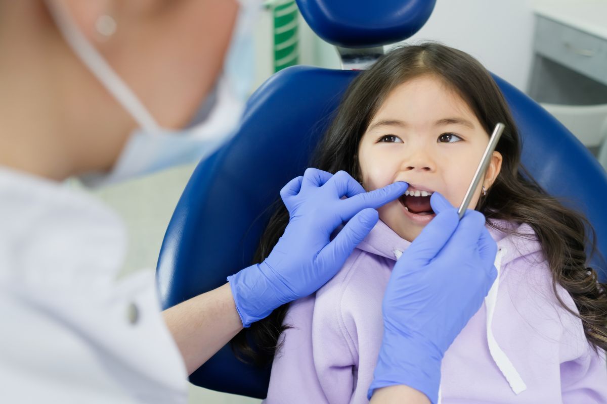 Young girl in dental chair receiving oral examination from dentist wearing blue gloves.