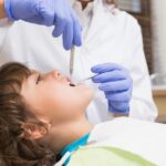 Pediatric patient receiving dental examination with dentist using instruments and wearing blue gloves.