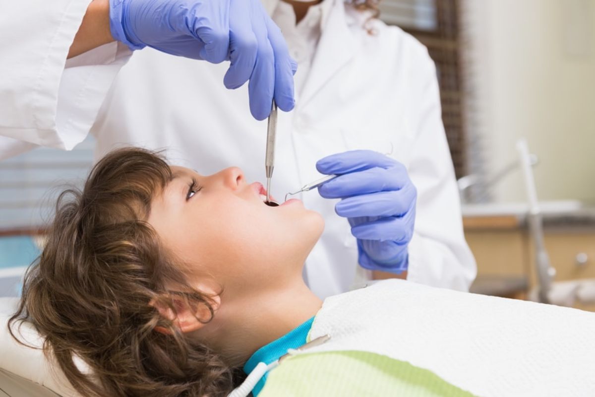 Pediatric patient receiving dental examination with dentist using instruments and wearing blue gloves.