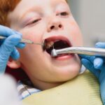Young patient receiving dental examination with mirror and explorer tool during checkup.