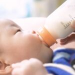 Infant drinking from bottle with measurement markings during feeding demonstration.