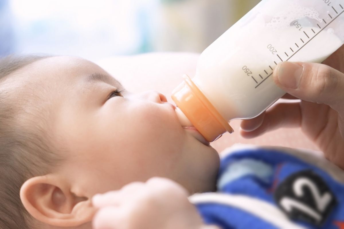 Infant drinking from bottle with measurement markings during feeding demonstration.