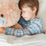 Child sleeping peacefully while hugging a teddy bear, illustrating healthy sleep patterns.