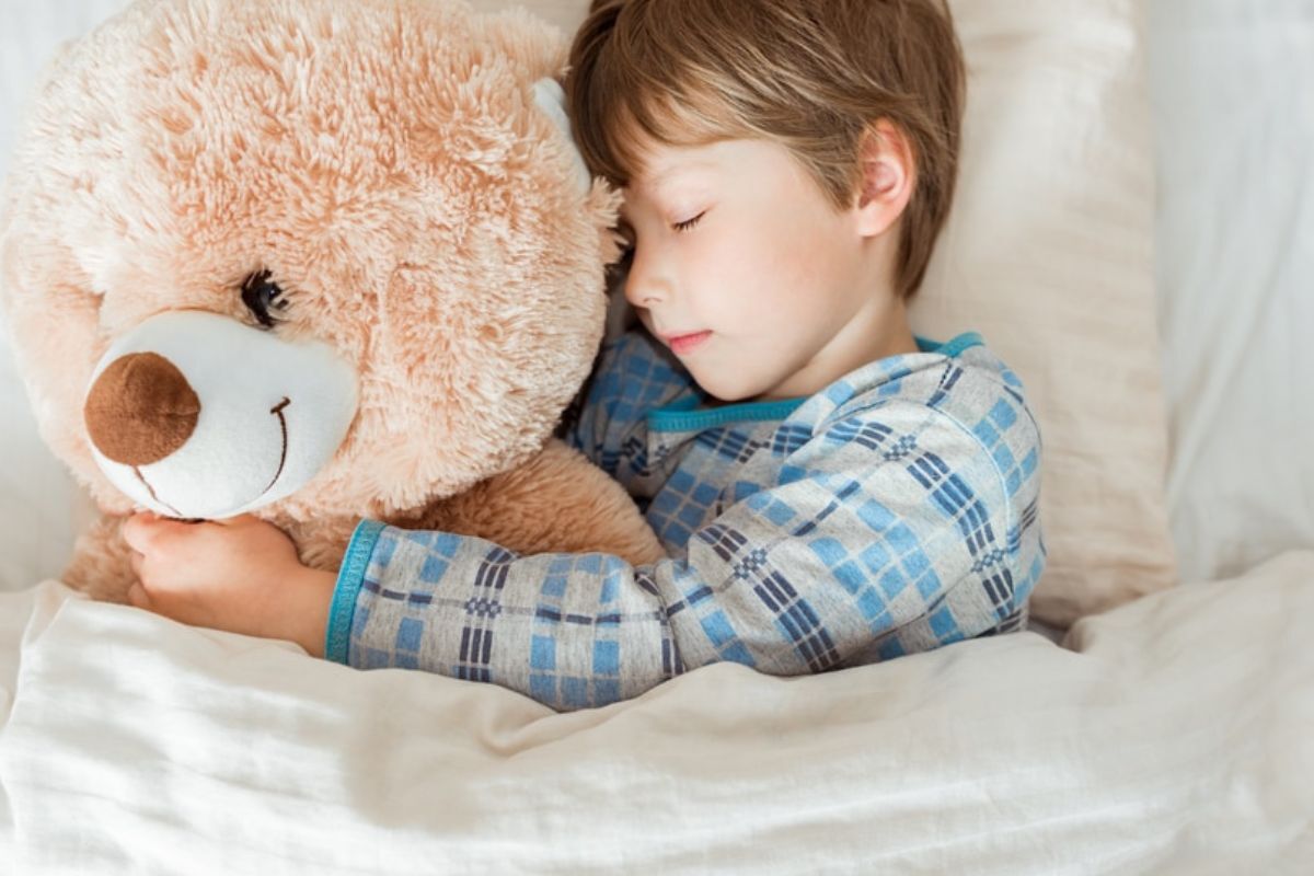 Child sleeping peacefully while hugging a teddy bear, illustrating healthy sleep patterns.
