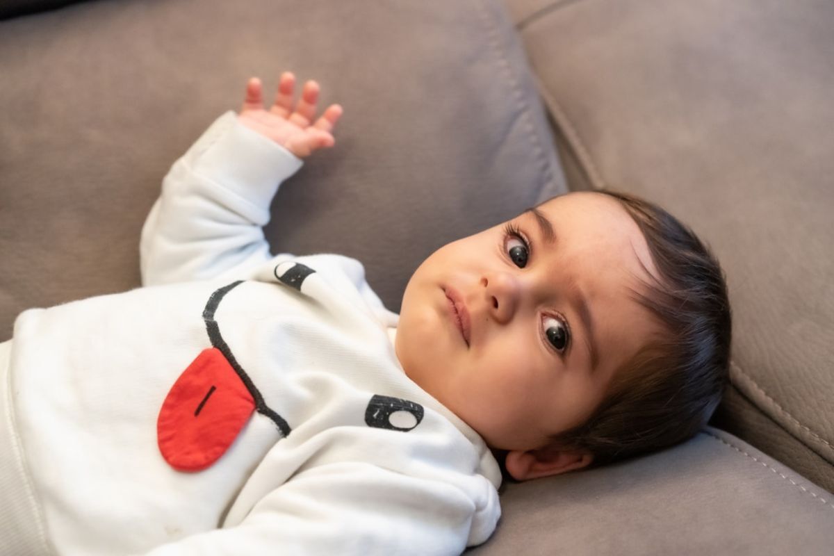 Infant in white outfit with red heart detail lying on gray couch.