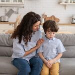 Mother talking with young boy about dental health on couch at home.