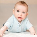 Smiling baby in light blue shirt discovering first teeth and gums.