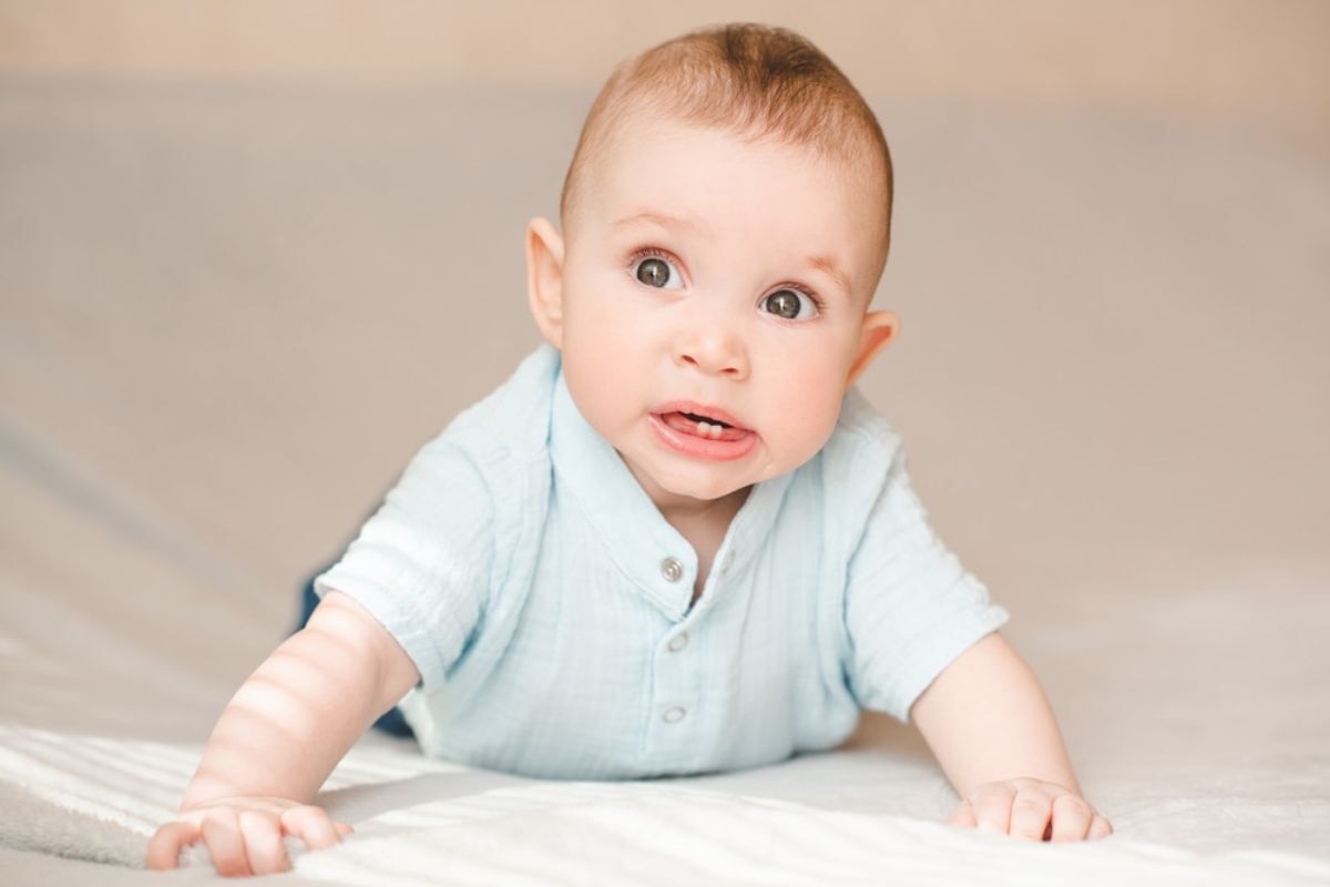Smiling baby in light blue shirt discovering first teeth and gums.