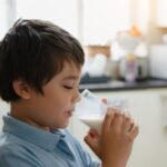 Young boy drinking milk from a glass in a kitchen setting.