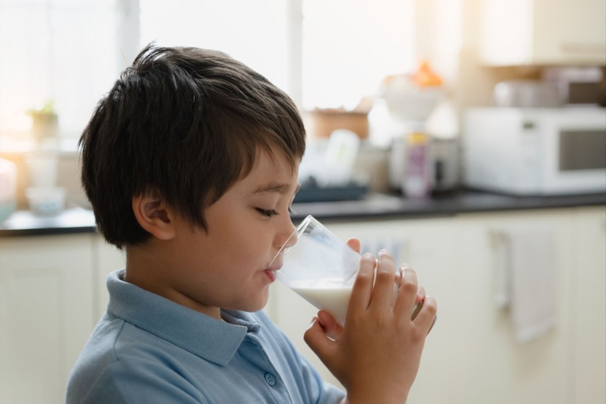 Young boy drinking milk from a glass in a kitchen setting.