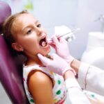Young girl receiving dental examination in treatment chair at pediatric dental office.