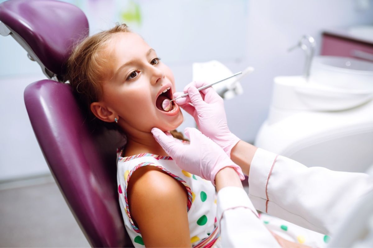 Young girl receiving dental examination in treatment chair at pediatric dental office.