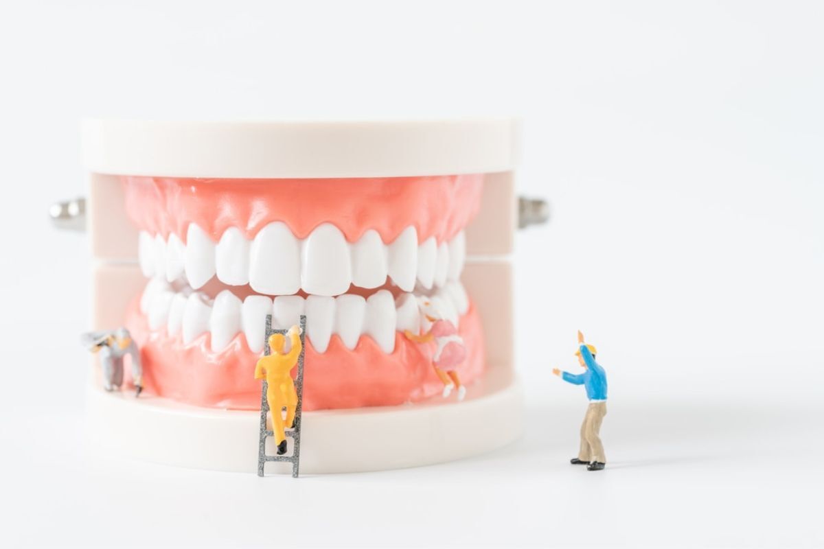 Miniature figures climbing a dental model showing teeth and gums for pediatric oral cancer screening education.