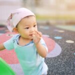 Happy toddler in pink hat sitting on colorful play mat, demonstrating healthy childhood development.