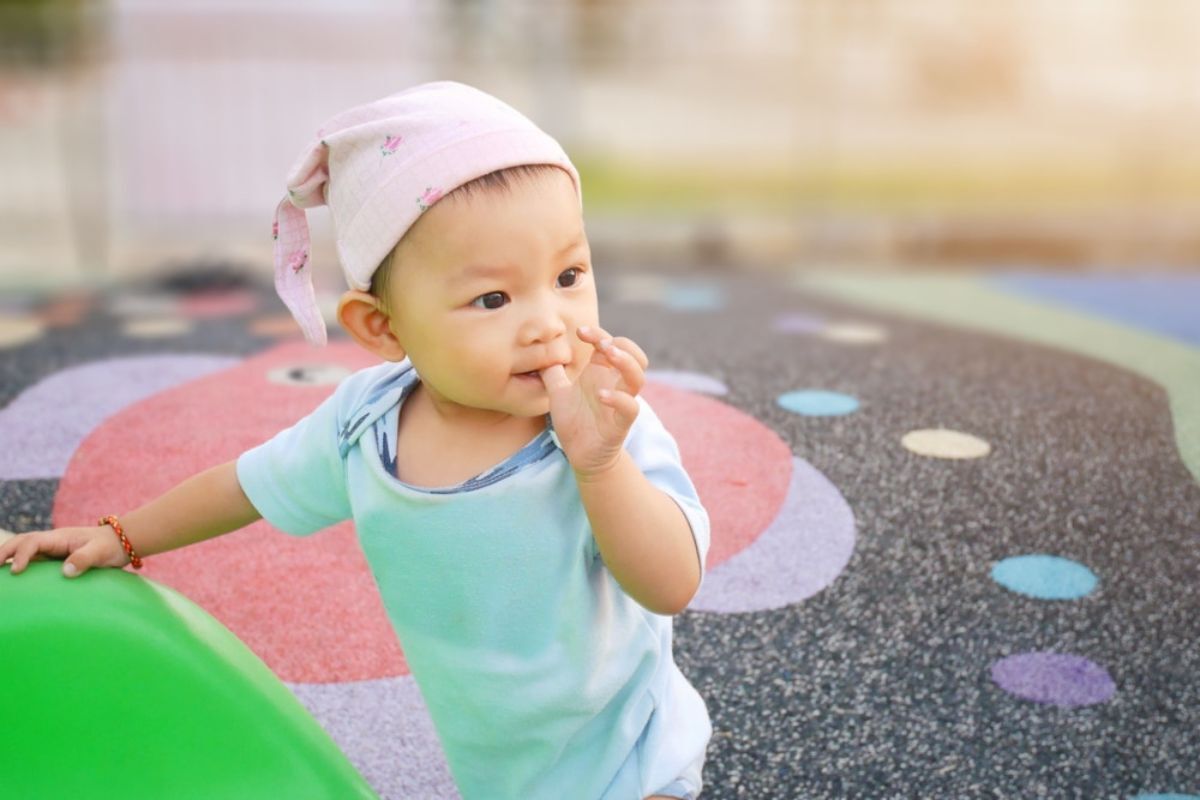 Happy toddler in pink hat sitting on colorful play mat, demonstrating healthy childhood development.