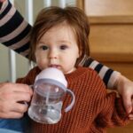 Toddler drinking from a sippy cup while held by parent, illustrating cavity risk from prolonged bottle use.