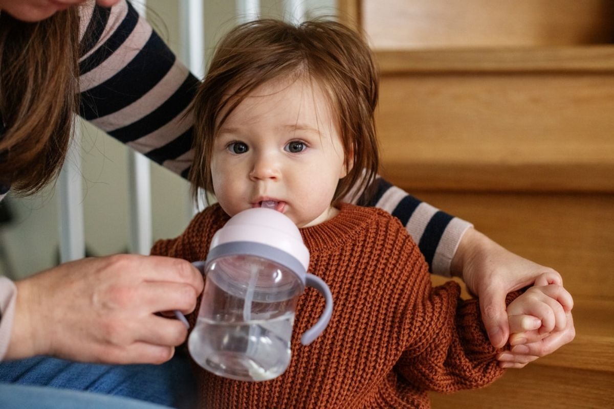 Toddler drinking from a sippy cup while held by parent, illustrating cavity risk from prolonged bottle use.