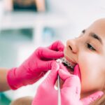 Orthodontist adjusting metal braces on patient's teeth during dental appointment.
