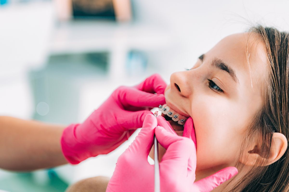 Orthodontist adjusting metal braces on patient's teeth during dental appointment.