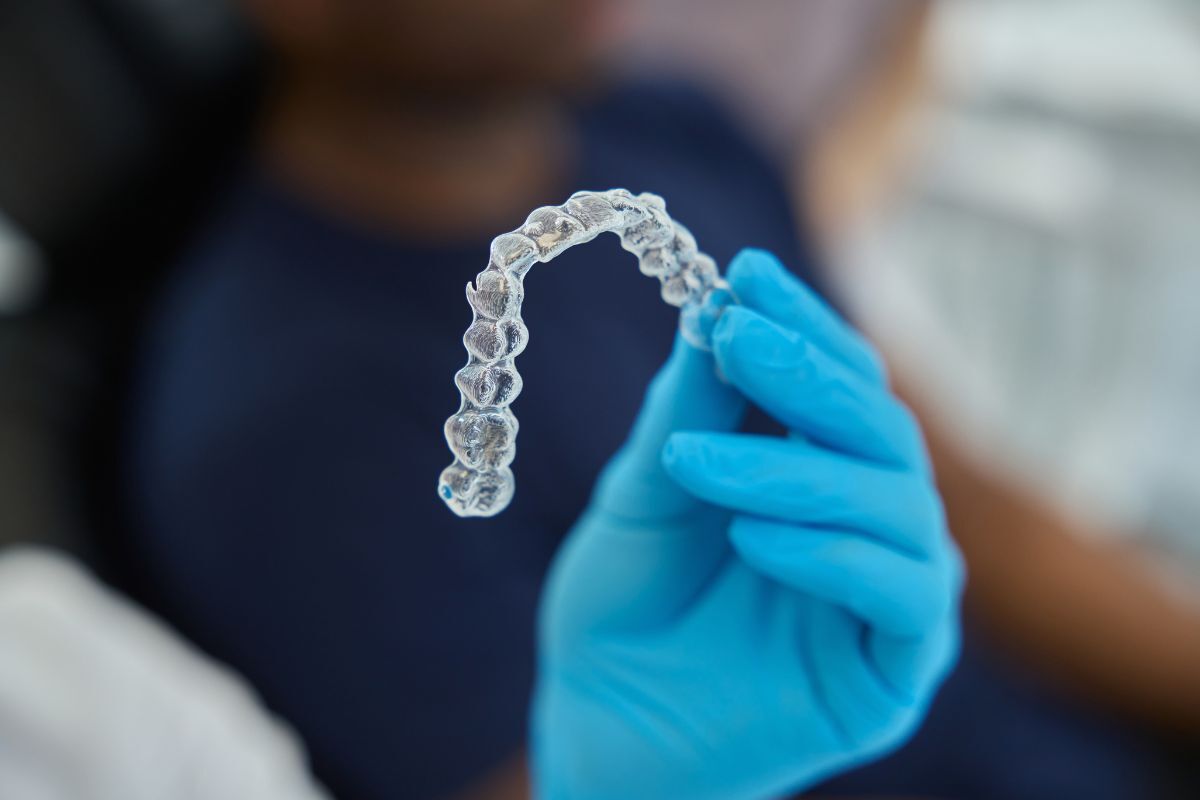 Clear aligners held in gloved hand showing individual dental trays for teeth straightening treatment.