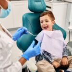 Young child smiling in dental chair while dentist provides pediatric gum care in Spring, TX.