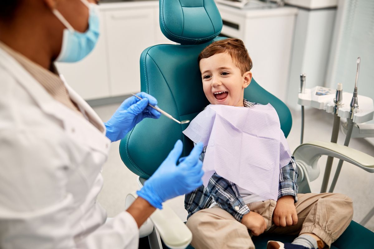 Young child smiling in dental chair while dentist provides pediatric gum care in Spring, TX.