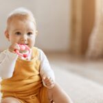 Happy baby in yellow outfit chewing on pink teething toy.