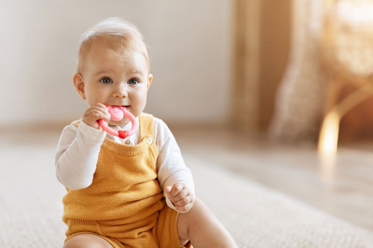 Happy baby in yellow outfit chewing on pink teething toy.