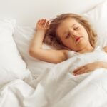 Young child sleeping peacefully in white bedding, demonstrating healthy sleep habits for managing apnea symptoms.