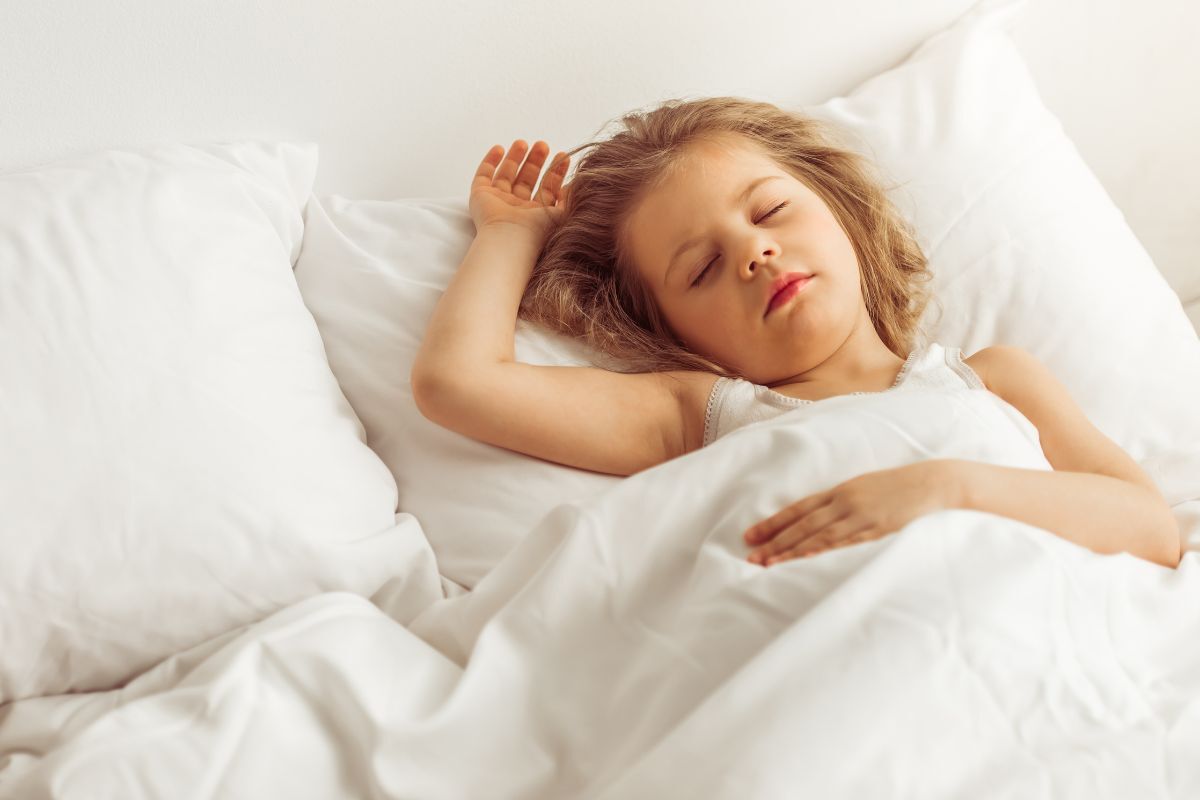 Young child sleeping peacefully in white bedding, demonstrating healthy sleep habits for managing apnea symptoms.
