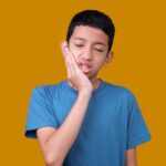 Boy holding his cheek in pain, illustrating TMJ discomfort in children.